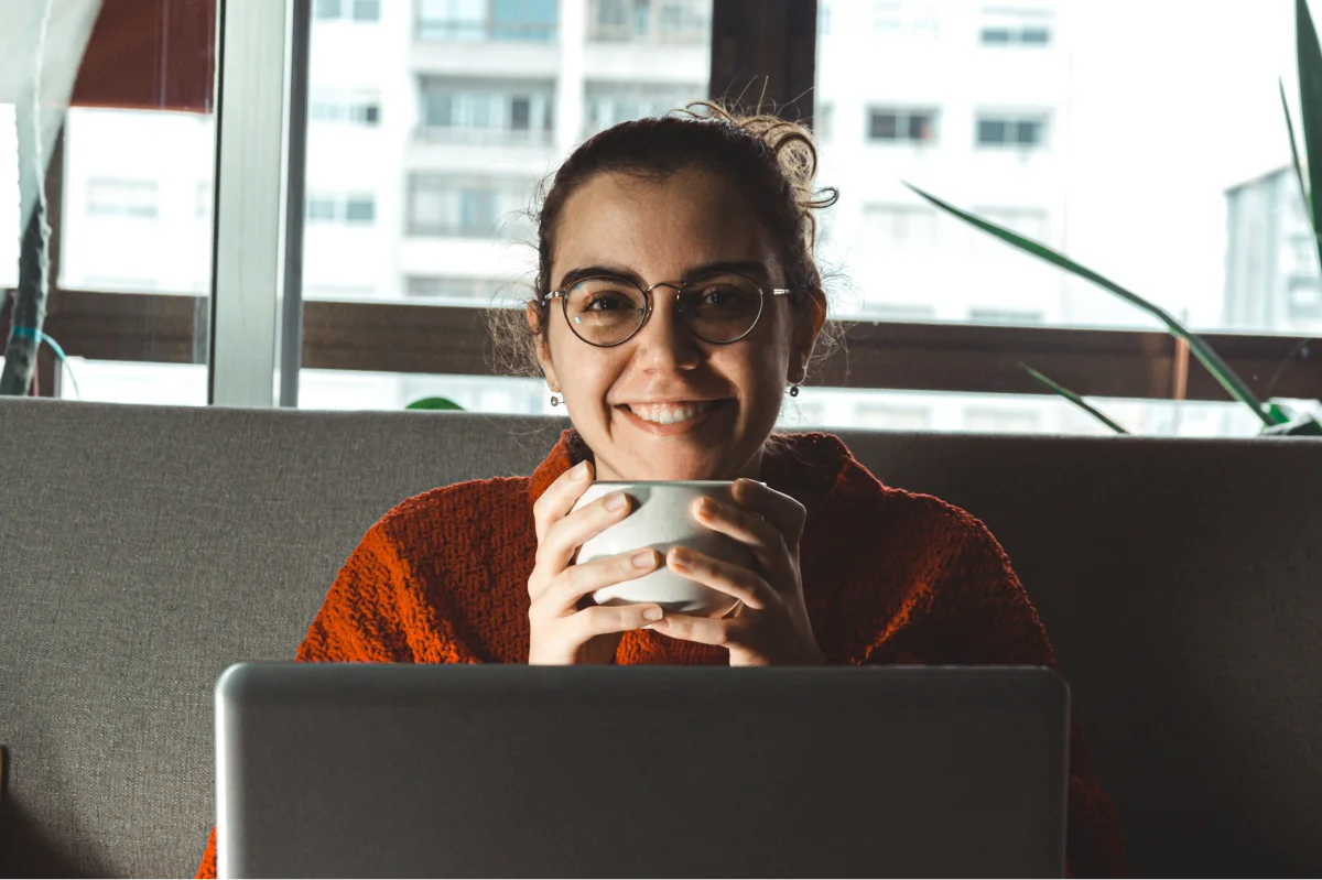 women smiles holding mug sitting behind a laptop
